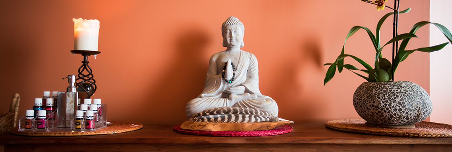 Buddha statue, candle and orchid on a wooden shelf against a warm orange wall