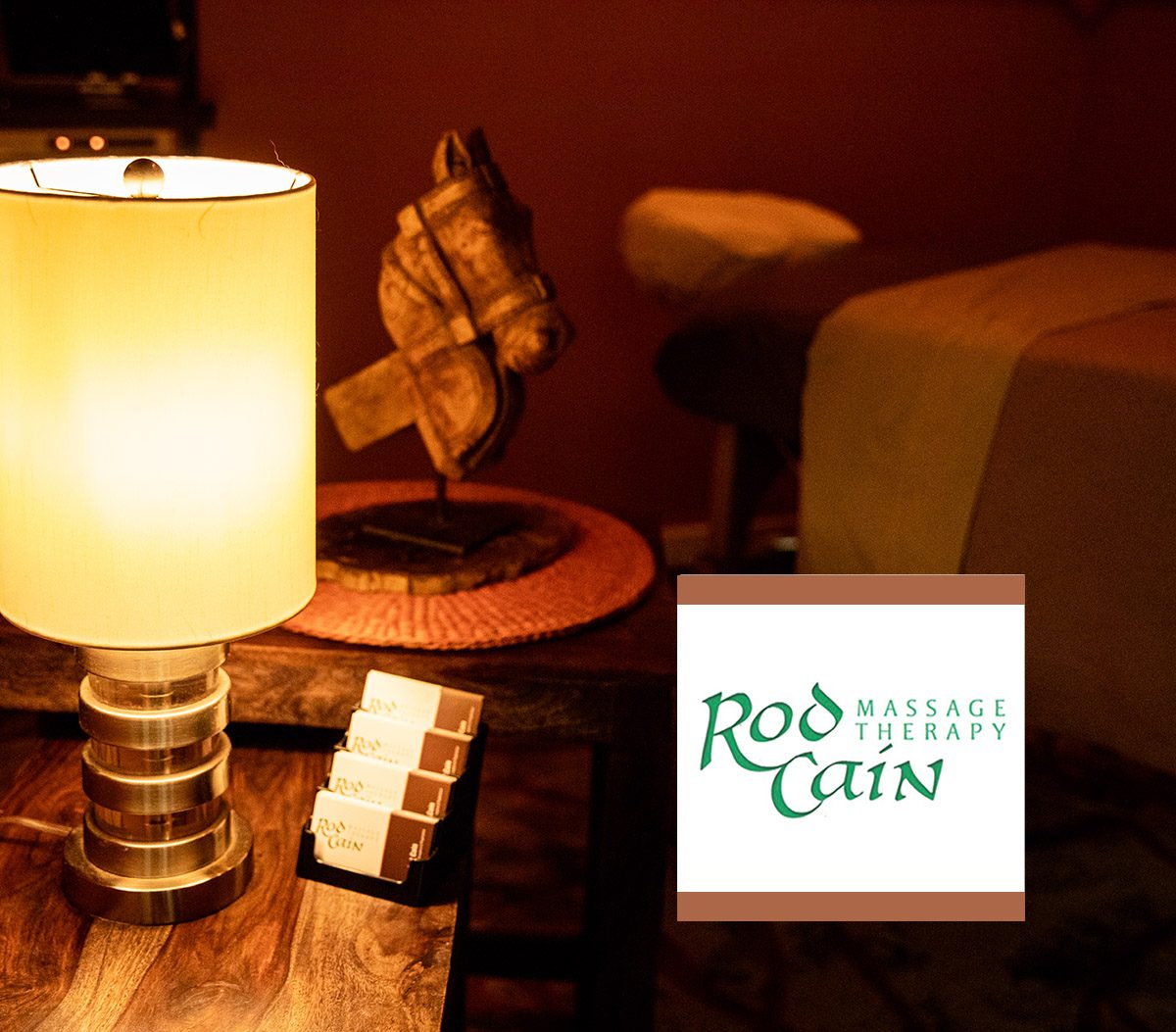 Treatment room with a glowing lamp, horse head sculpture and the Rod Cain Massage Therapy sign beside a massage table
