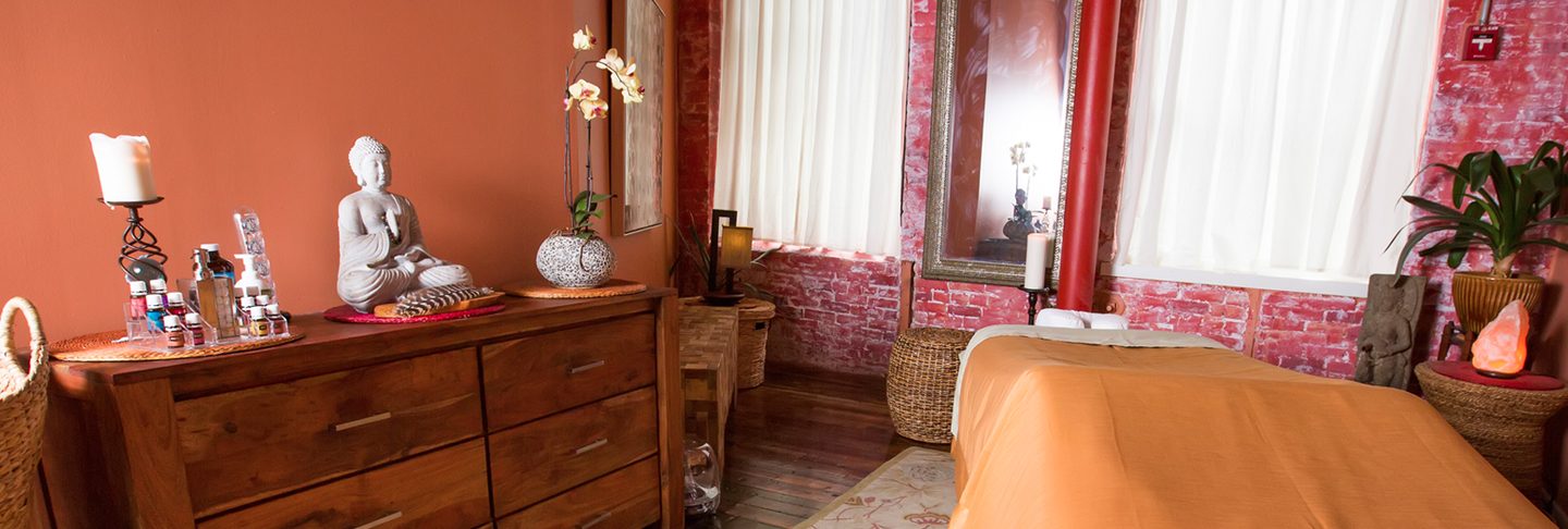Massage room in our Burlington studio with a massage table, wooden dresser and warm curtains